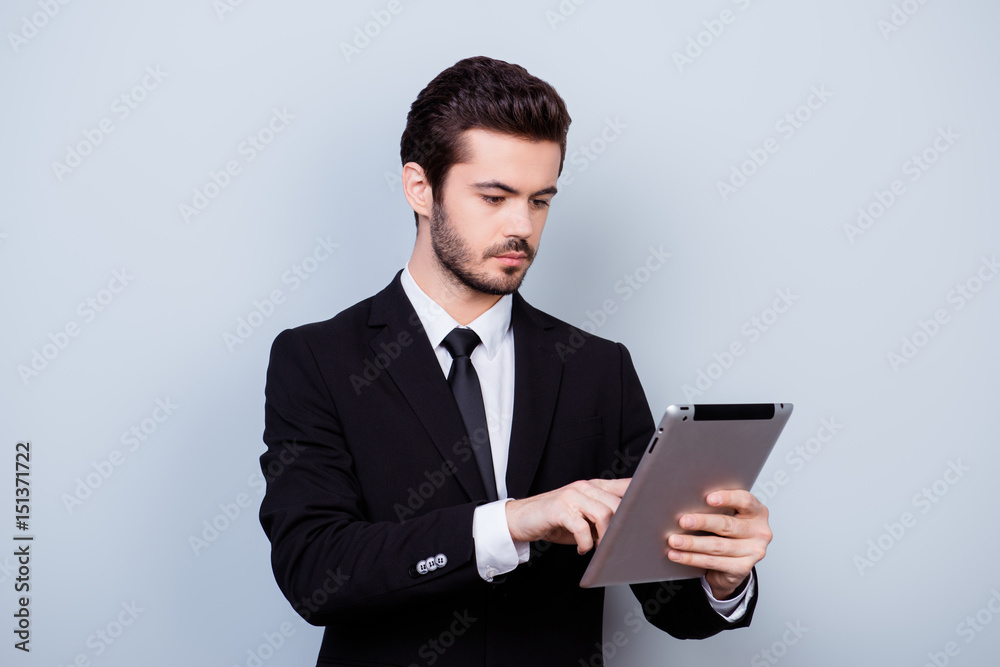 Young serious smart guy in formal clothes holding digital tablet and reading useful information from it Young serious smart guy in formal clothes holding digital tablet and reading useful information from it