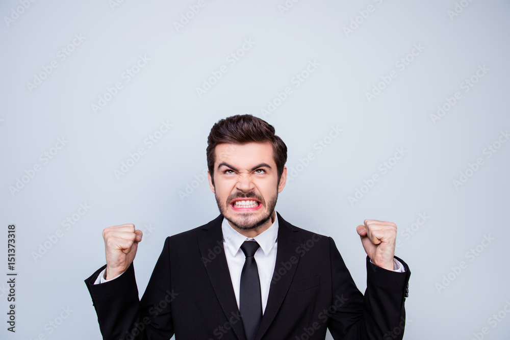 Young very angry man in black suit showing fists and looking up on copyspace over his head in rage Young very angry man in black suit showing fists and looking up on copyspace over his head in rage