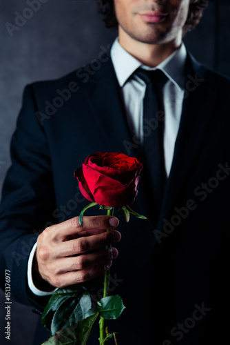 Cropped photo of business man holding a red rose in his hand. He is wearing formal wear