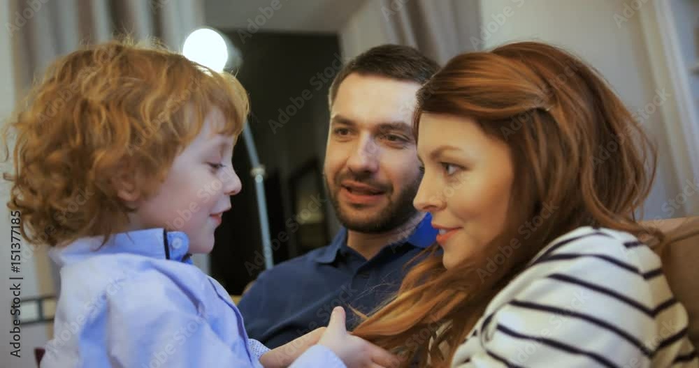 Happy family sitting together at the couch at the living room. Father, mother and son sitting on the sofa, relaxing, playing games and talking. Son is telling an interesting story to his parents and Happy family sitting together at the couch at the living room. Father, mother and son sitting on the sofa, relaxing, playing games and talking. Son is telling an interesting story to his parents and