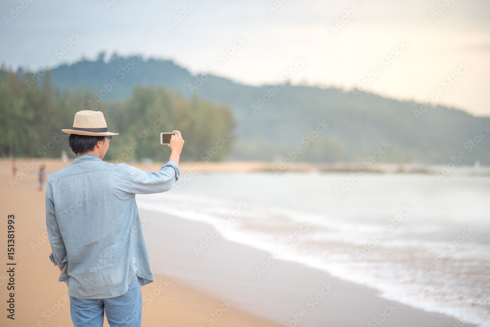 young Asian happy man with jean shirt and hat taking photos on tropical beach island by smartphone, summer holiday or vacation travel concepts young Asian happy man with jean shirt and hat taking photos on tropical beach island by smartphone, summer holiday or vacation travel concepts