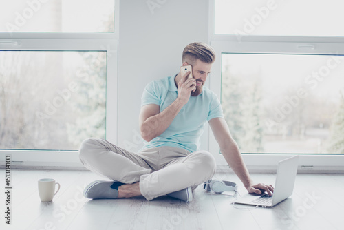 A portrait of a young man working at home at relaxed atmosphere. He is talking on the phone, typing on laptop and smiling photo