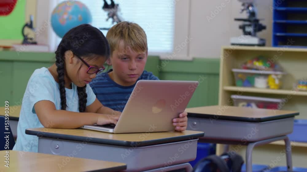 Two kids in school classroom working on laptop computer