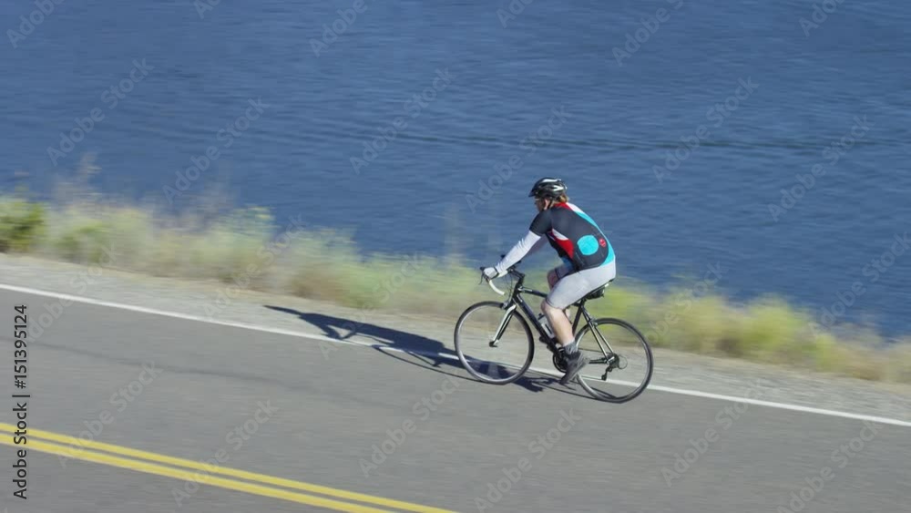 Man riding bicycle on country road overlooking lake Man riding bicycle on country road overlooking lake