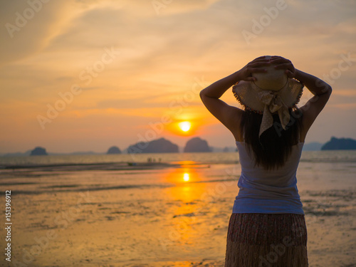 Woman wearing hat with open arms under the sunrise near the sea