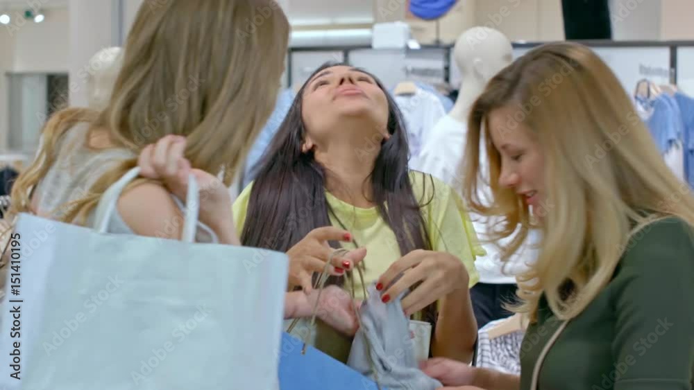 Medium shot of laughing Hispanic woman and her Caucasian female friends with blond hair looking at purchased blouse and chatting with excitement Medium shot of laughing Hispanic woman and her Caucasian female friends with blond hair looking at purchased blouse and chatting with excitement
