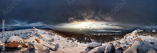 Ural Mountains. Sunset in the Ural mountains. Stones and slopes with snow. The sun goes behind a cloud. The wide panorama around.
