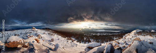 Ural Mountains. Sunset in the Ural mountains. Stones and slopes with snow. The sun goes behind a cloud. The wide panorama around. photo