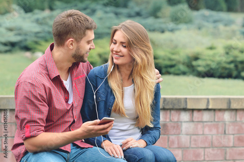 Couple listening to the music with earbuds from a smart phone in a park.