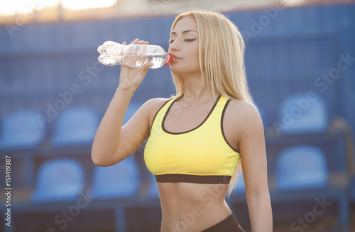 Slim young woman drinking water after training