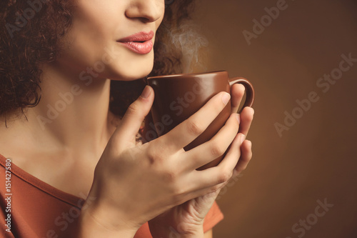 Portrait of young beautiful woman with cup of coffee on brown background