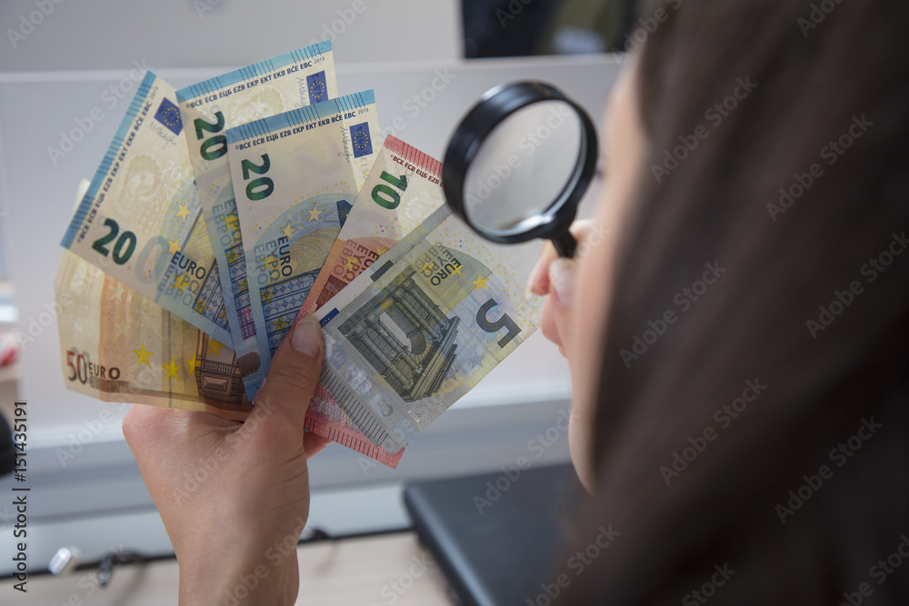 Φωτογραφία Business woman uses a magnifying glass to check the originality of money