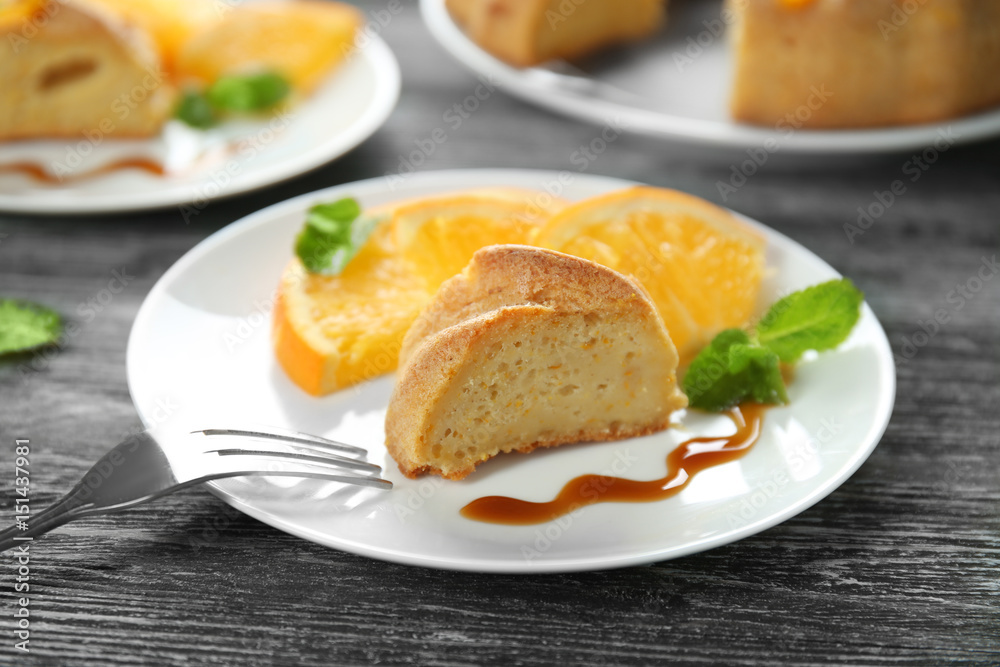 Plate with piece of citrus cake and fresh orange slices on wooden table Plate with piece of citrus cake and fresh orange slices on wooden table