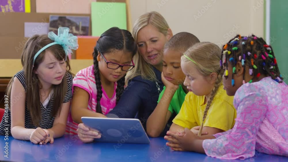 Teacher and group of students look at digital tablet together in school classroom