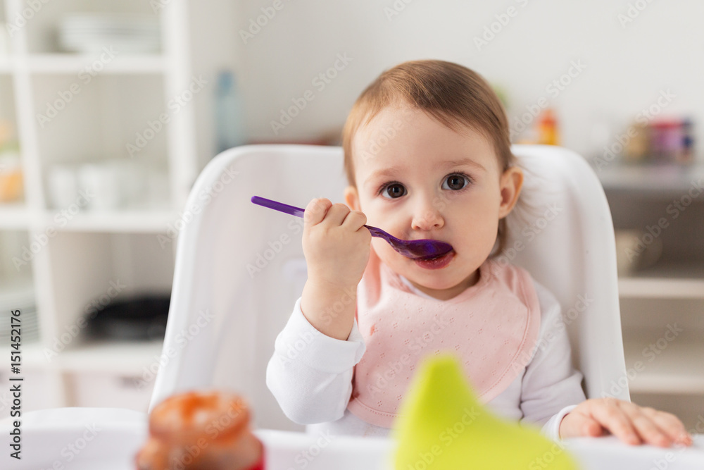 baby girl with spoon eating puree from jar at home baby girl with spoon eating puree from jar at home