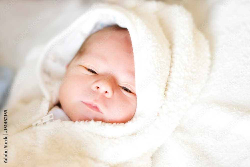 A real seven-day newborn baby wrapped in a white terry towel opened his eyes A real seven-day newborn baby wrapped in a white terry towel opened his eyes