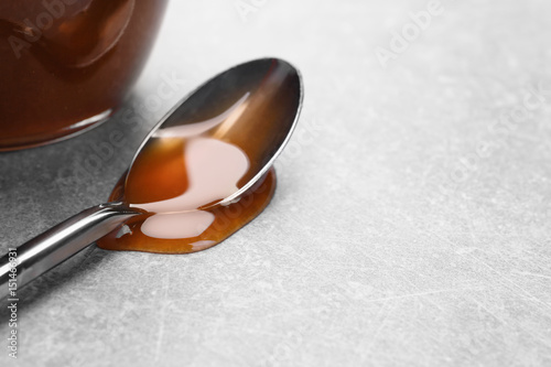 Spoon with tasty caramel sauce on light background, closeup