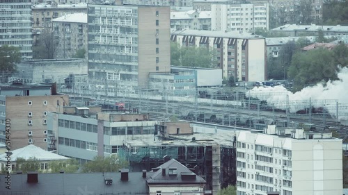 View from distance of big railway terminal and old vintage locomotive blowing a lot of smoke while passing through railway station district, puffer on railroad during Victory's day in Moscow, Russia