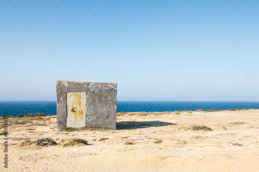 Illegally constructed concrete shelter on limestone cliffs in Gozo, Malta close to wied il-mielah. Barren landscape with the sea and blue sky.