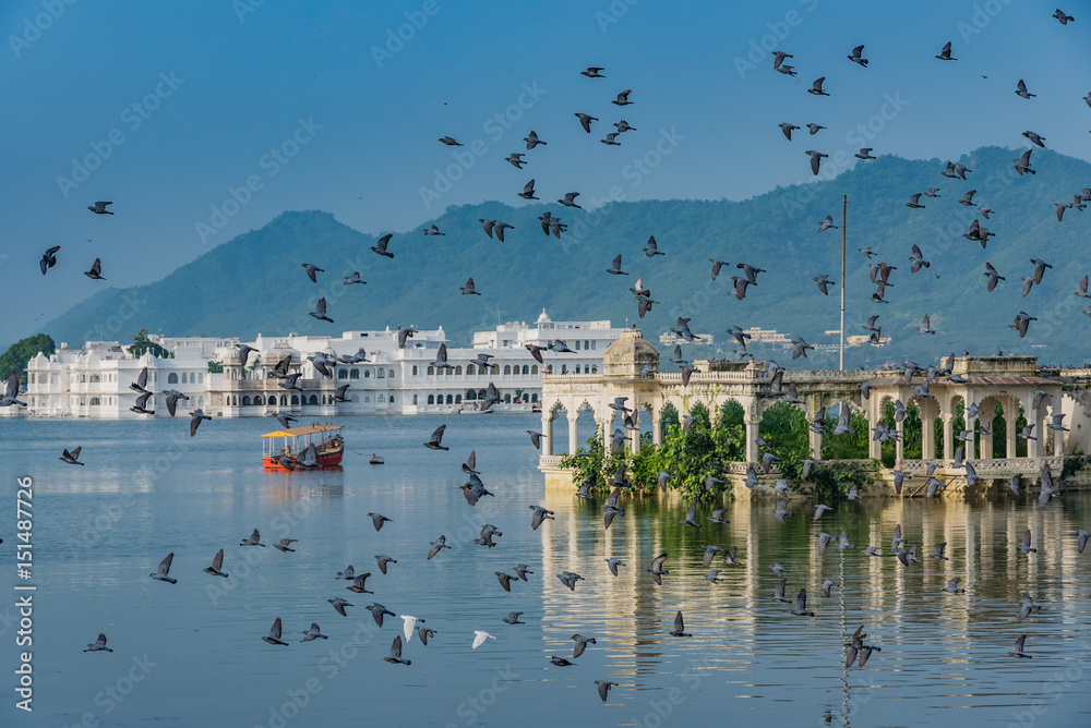 Udaipur's Lake Palace in the middle of Lake Pichola with birds flying in the backdrop of distant hills in the morning.
