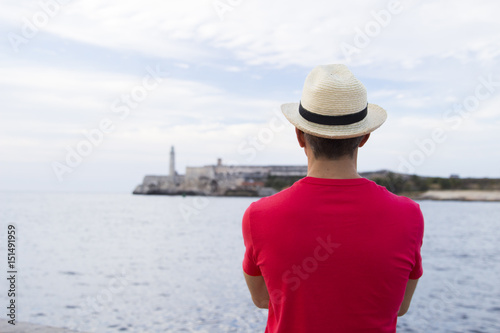 Man stands with his back to us in white hat and on the background Morro Castle  © Alla