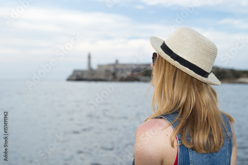 Woman sits on the embankment in Havana and Morro castle on the background © Alla