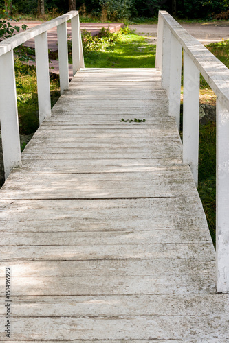 Old wooden painted white paint bridge in sunny summer forest.