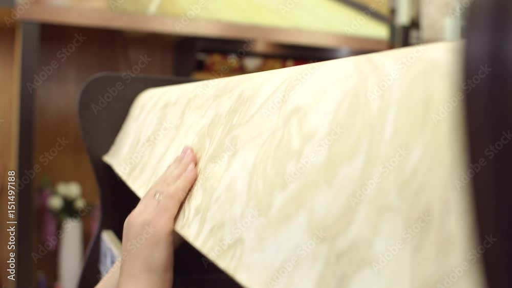 Woman is wringing a roll of wallpaper, close-up. Girl chooses wallpaper in the building store. Woman is wringing a roll of wallpaper, close-up. Girl chooses wallpaper in the building store.