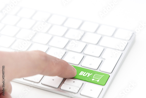 finger pressing a green key labeled BUY with shopping cart symbol on a computer keyboard concept