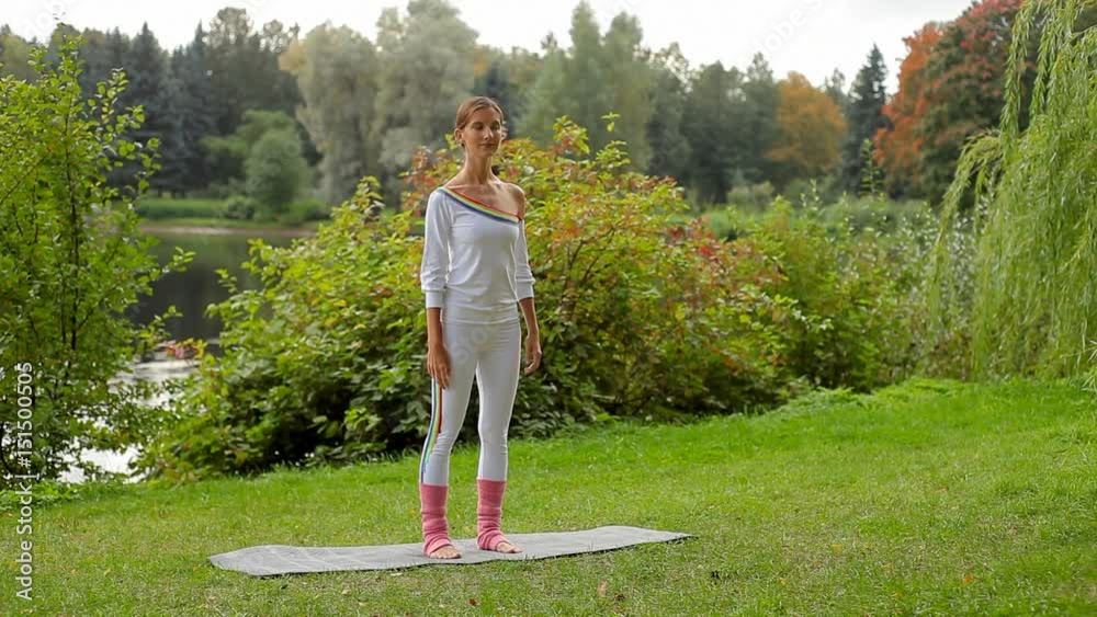 Young woman does yoga exercise standing on a non slip mat at a river bank Young woman does yoga exercise standing on a non slip mat at a river bank