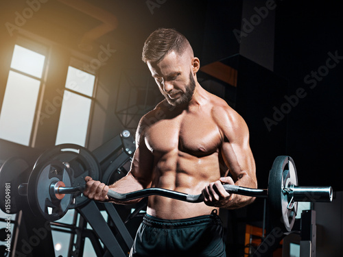 Portrait of super fit muscular young man working out in gym with barbell