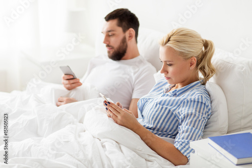 couple with smartphones in bed at home