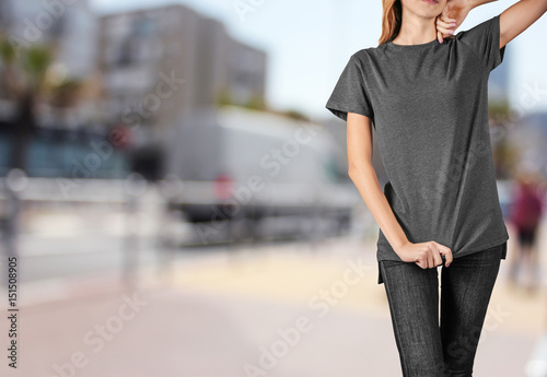 Young woman in blank grey t-shirt standing against textured wall, close up © Africa Studio