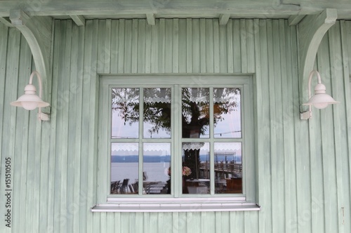 White vintage window in a white-green painted wooden house wall with reflexions of surrounding items
