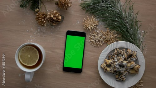 Male hand using smart phone with green screen. Finger tapping and scrolling pages on touchscreen. Christmas decor on wooden table background. Chroma key. top view photo