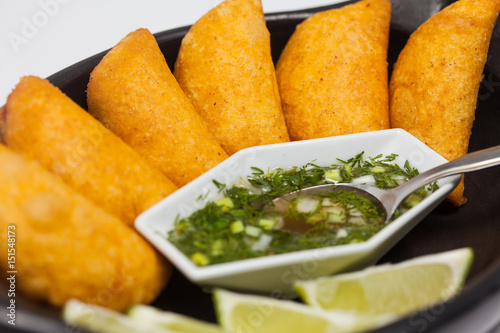 Typical Colombian empanadas served with spicy sauce on traditional black ceramic dish
