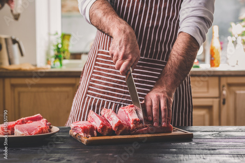 Man cuts of fresh piece of beef on a wooden cutting board in the home kitchen