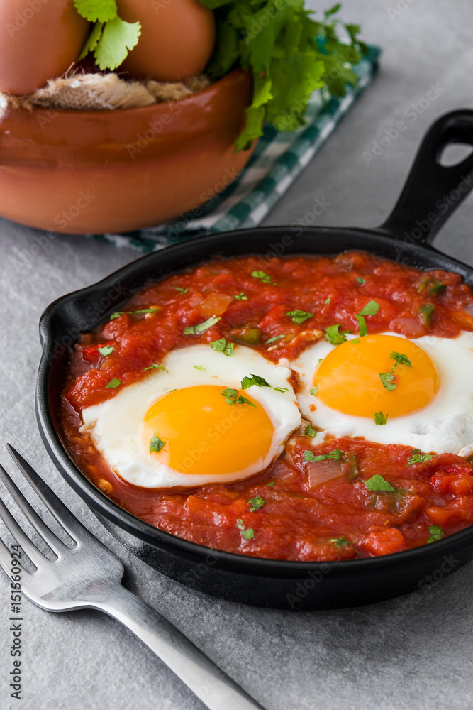 Mexican breakfast: Huevos rancheros in iron frying pan on gray stone
