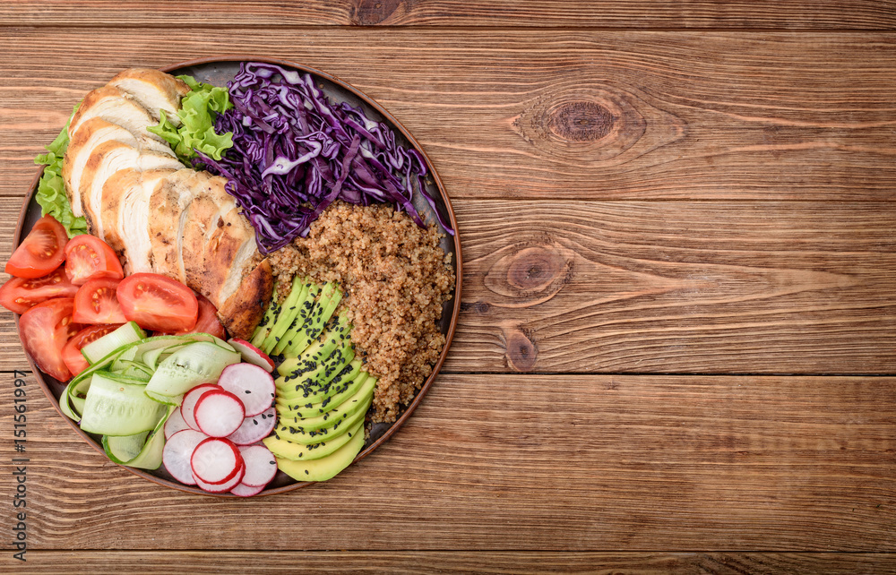 Healthy salad bowl with quinoa, chicken, avocado and vegetables on wooden background .
Healthy salad bowl with quinoa, chicken, avocado and vegetables on wooden background .