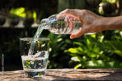 Female hand pouring water from bottle to glass on nature background