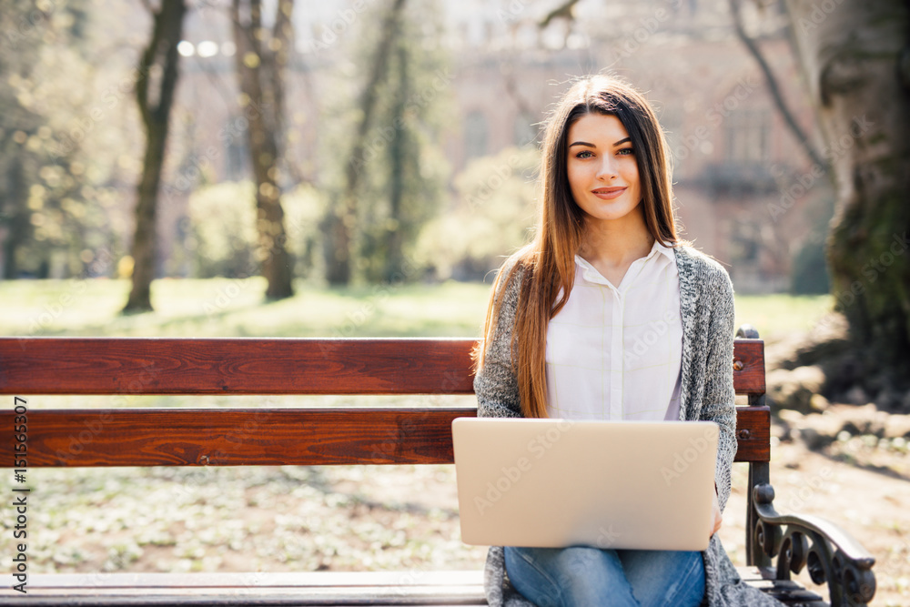 Girl using a laptop on a bench in park