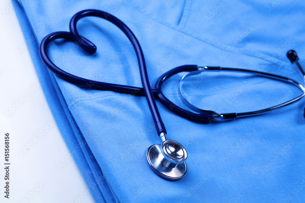 Medical stethoscope twisted in heart shape lying on patient medical history list and blue doctor uniform closeup Medical stethoscope twisted in heart shape lying on patient medical history list and blue doctor uniform closeup