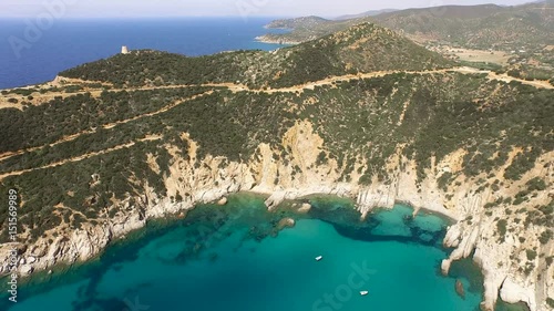 Drone fly over sardinia coastline and colorful turquoise mediterranean sea surraunded by high cliff and ancient ruins of a watchtower