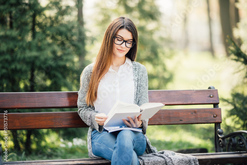 serious young, beautiful girl holding an open book, read background summer green park