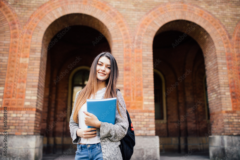 smiling teenage girl with folders and bag in university background