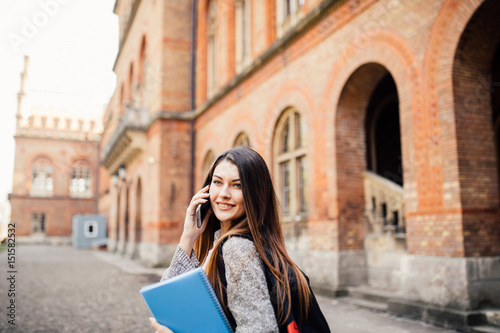 Single student walking and speak mobile phone with a university building in the background photo