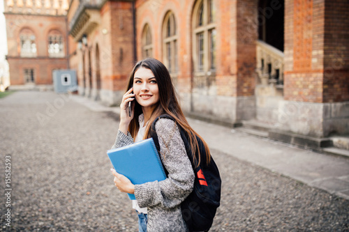 Single student walking and speak mobile phone with a university building in the background photo