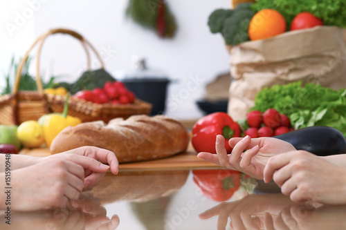 Two women discussing a new menu in the kitchen, close up. Human hands of two persons gesticulating at the table among fresh vegetables. Cooking and friendship concept.