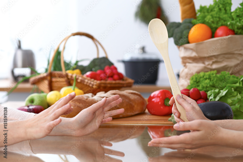 Two women discussing a new menu in the kitchen, close up. Human hands of two persons gesticulating at the table among fresh vegetables. Cooking and friendship concept.
