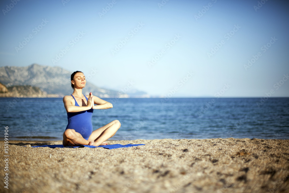 Young pregnant woman enjoying in yoga meditation on beach